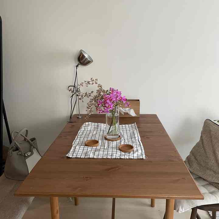 ナチュラルカラーと白を基調としたキッチン空間、木製ダイニングテーブルに花瓶とリネン布が配置されたシンプルなインテリア