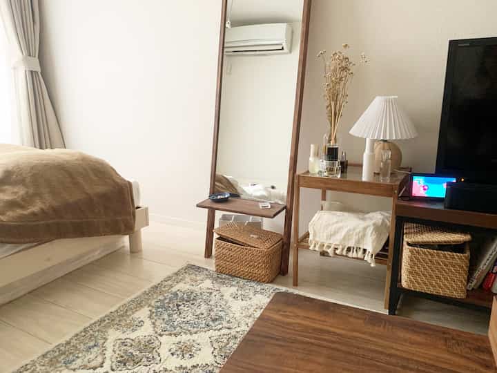 暖かみのあるベージュとナチュラルな木目調の落ち着いた寝室、木製の鏡とラタンバスケットが配置されたインテリア