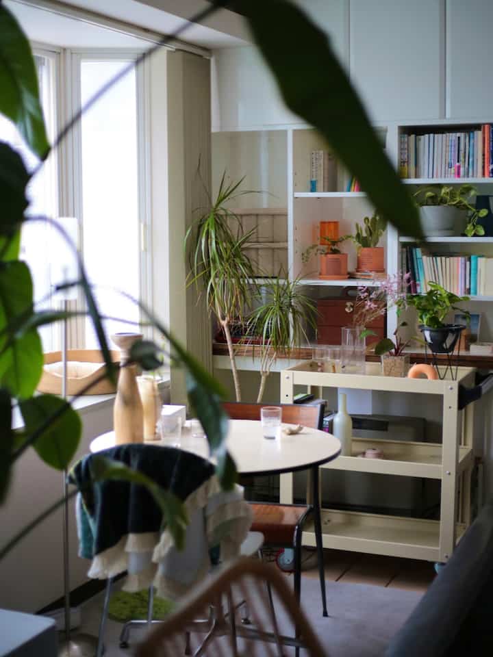 White and brown toned living room featuring a round table, kitchen cart, shelves, and plants in a natural setting