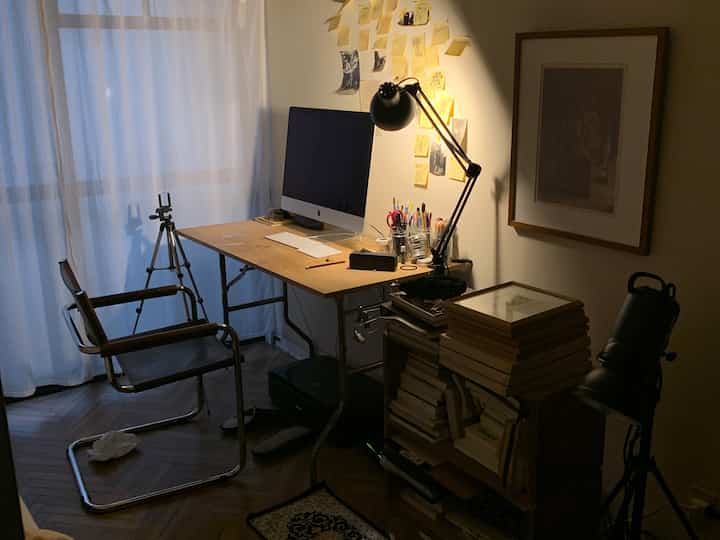 柔らかな木目調と白いカーテンが調和するコンパクトなホームオフィス、デスク上にコンピューターとテーブルランプが配置された雰囲気のあるインテリア