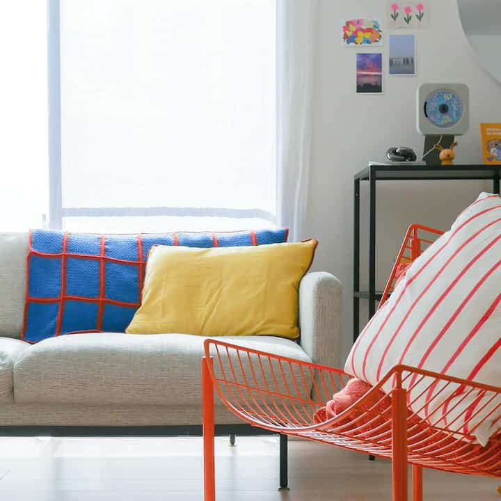 ホワイトトーンのリビングに、ナチュラルなベージュのソファとオレンジのメタルアームチェアが配置された雰囲気のあるインテリア