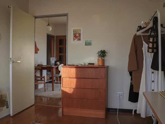Warm wood tone studio apartment featuring a wooden dresser and clothes rack with a natural and vintage atmosphere
