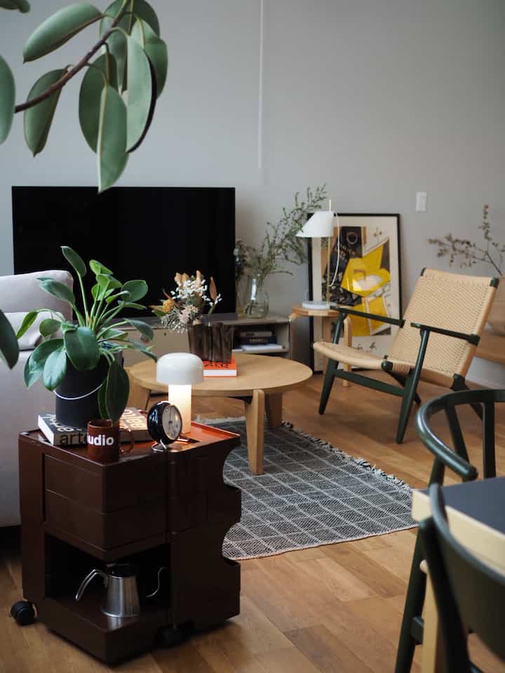 Natural-toned living room featuring a wooden round table, brown Bobby Wagon cart, and natural material armchair creating a cozy atmosphere
