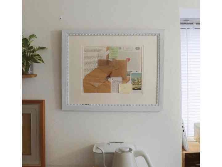 白とナチュラルカラーのキッチン空間、電気ケトルと額縁、植物が配置された印象的なインテリア