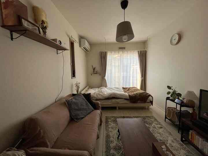 ベージュとブラウンのトーンが特徴の6畳の寝室兼リビング、ソファとベッドが配置された落ち着いた空間