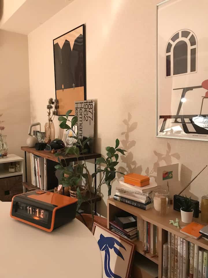 温かみのあるベージュ色の壁と木製の棚があるカフェ風の空間、ポスターと植物が配置された雰囲気のあるインテリア