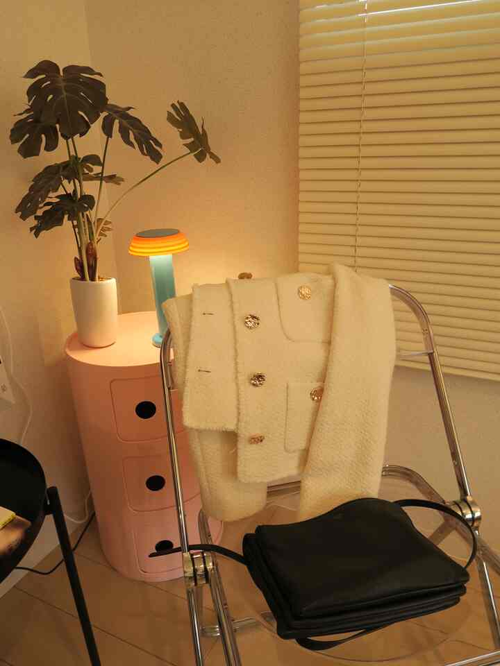 暖かい照明とピンクの収納があるコンパクトなミッドセンチュリーモダンの部屋、透明な椅子と植物が配置された居心地の良い空間