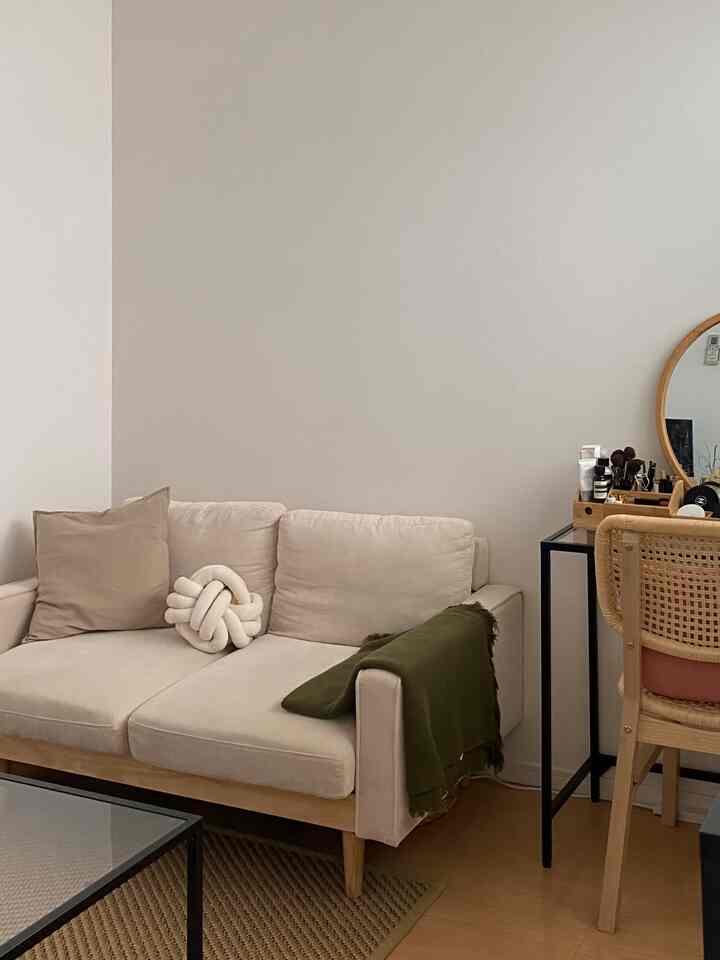 Beige and natural tone living room featuring a beige sofa, wooden framed chair, and black frame vanity in a cozy setting
