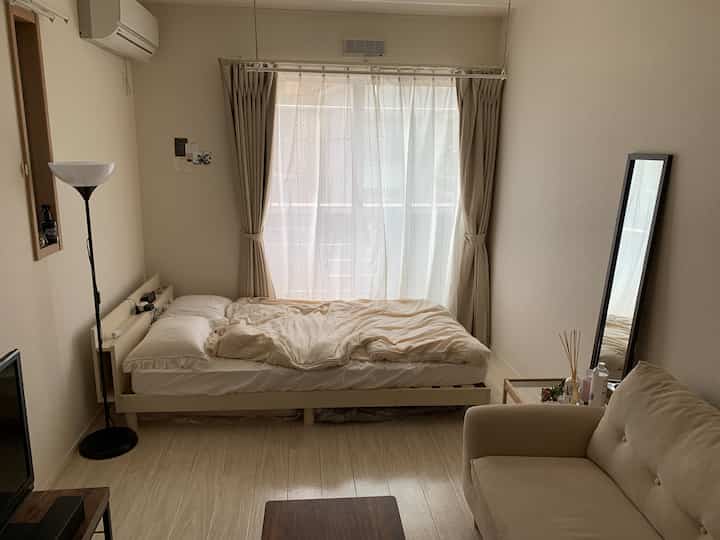 ベージュとホワイトトーンの小さな寝室、ベッドとベージュのソファが配置された落ち着いた空間