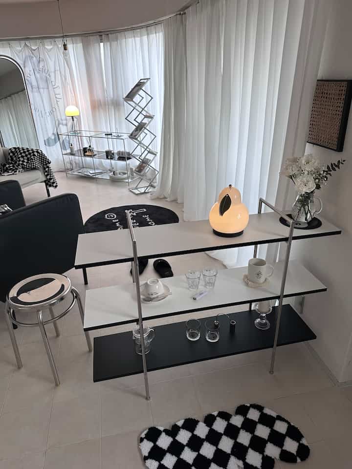 白とシルバーの配色が特徴的なリビング、ミニマルな棚とスツールが配置された印象的な空間