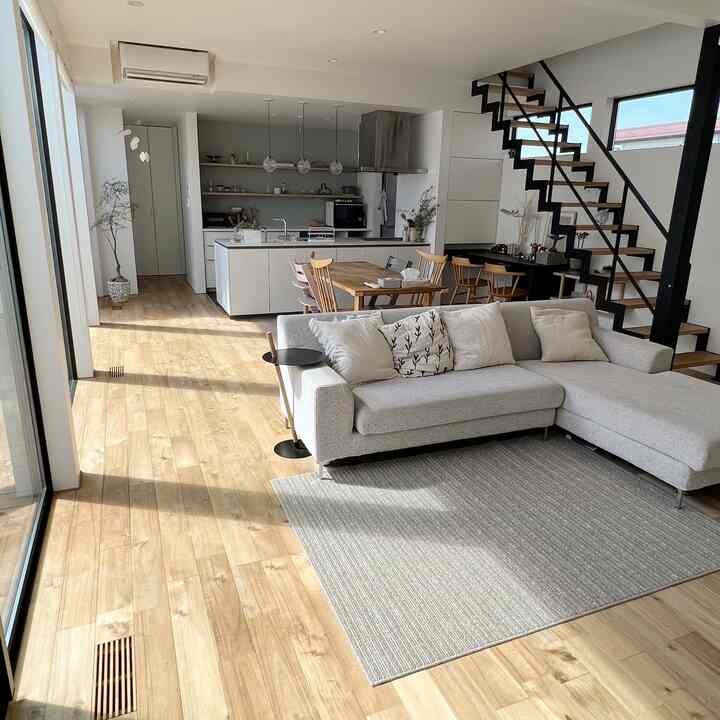 Natural color and wood-toned Nordic long narrow living room featuring a large sectional sofa, dining table, and visible stairs