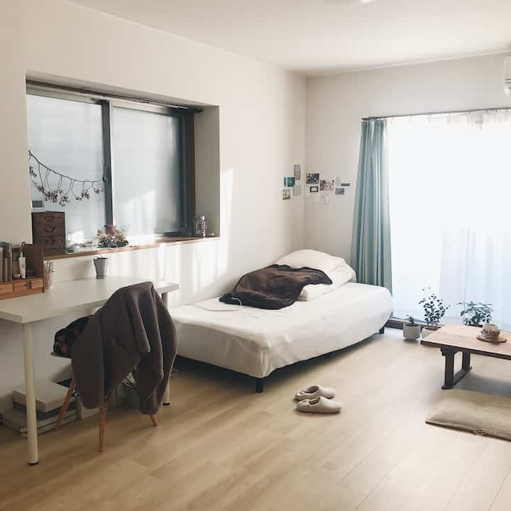 Bright white and wood tone single bedroom featuring low furniture and mint curtains with a simple, natural atmosphere