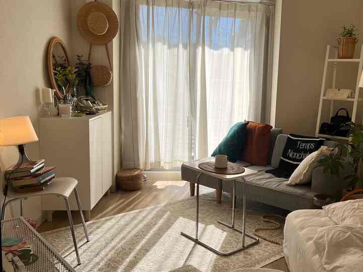 ナチュラルなベージュトーンのコンパクトなリビング、カラフルなクッションと陽光が差し込む窓、温かみのあるラグが印象的な空間