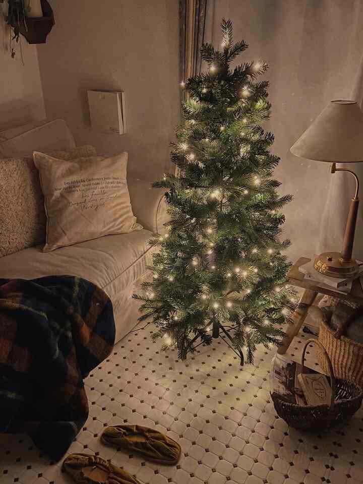 白と木目調が調和したリビング、ライトアップされたクリスマスツリーとソファ、テーブルランプが配置された雰囲気のあるインテリア