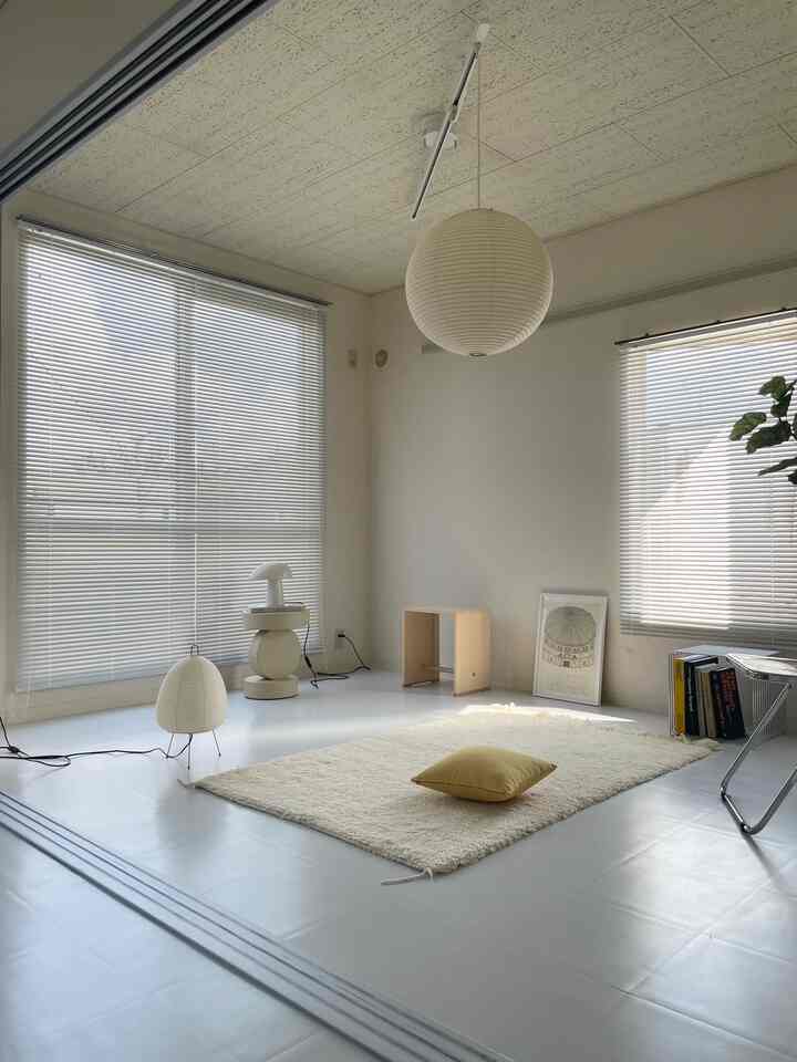 Modern natural living room in white and beige tones, featuring a large rug, pendant light, and wooden stool in a clean layout