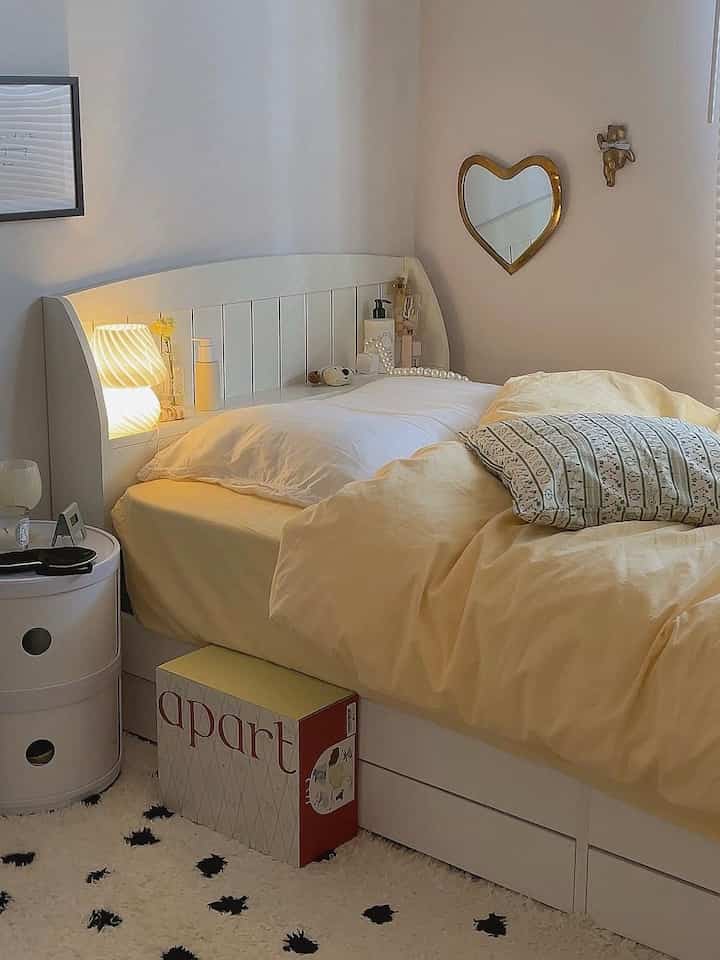 ホワイトの壁とベッドフレーム、イエローの寝具が配置されたコンパクトな寝室の印象的な空間