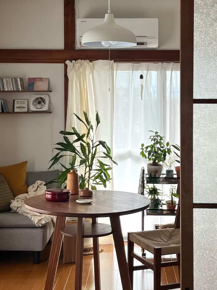 ナチュラルな色調のリビング、丸い木製ダイニングテーブルとソファ、多数の植物が配置された雰囲気のあるインテリア