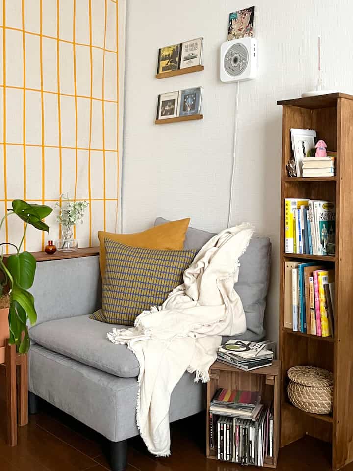 グレーとブラウンの色調が調和するリビング、一人掛けソファと木製の本棚、クッションとブランケットが落ち着いた雰囲気を醸し出す空間