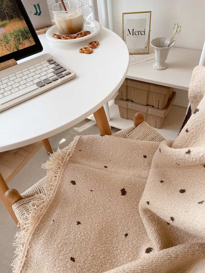 Cozy home office space featuring natural beige wooden desk with a comfortable blanket draped over a chair