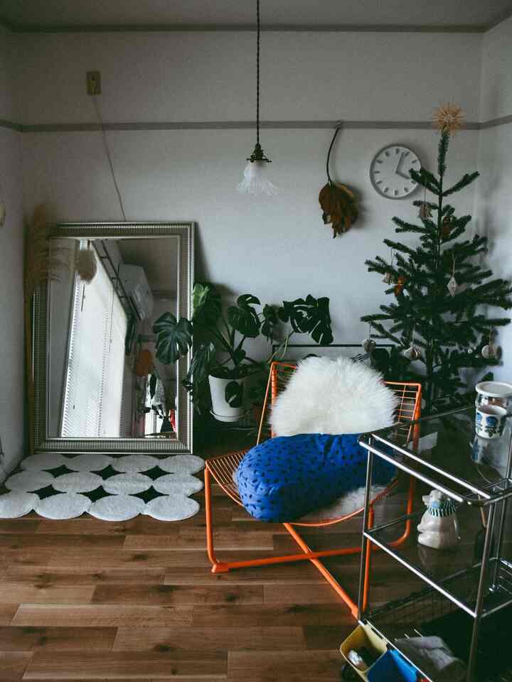 Modern living room with white walls and brown wooden flooring, featuring an orange armchair, Christmas tree, and large mirror
