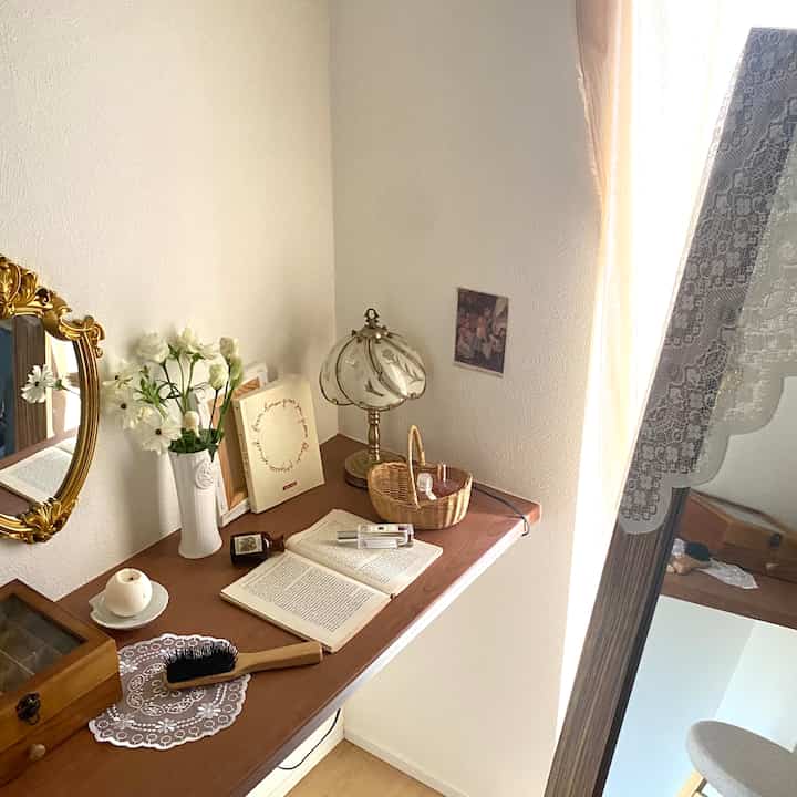 暖かい木目調と白い壁が調和したヴィンテージ風のコーナースペース、デスク上のヴィンテージランプと装飾的な鏡が落ち着いた雰囲気を醸し出すインテリア