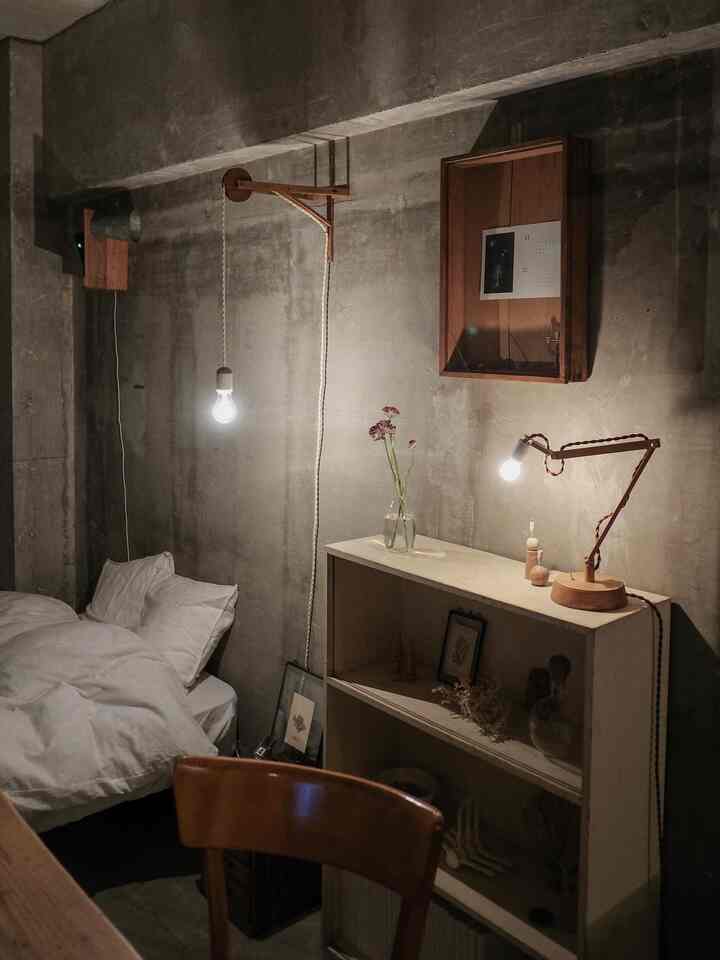 Gray concrete walls in a modern bedroom featuring wooden table lamp and pendant light in a cozy small room