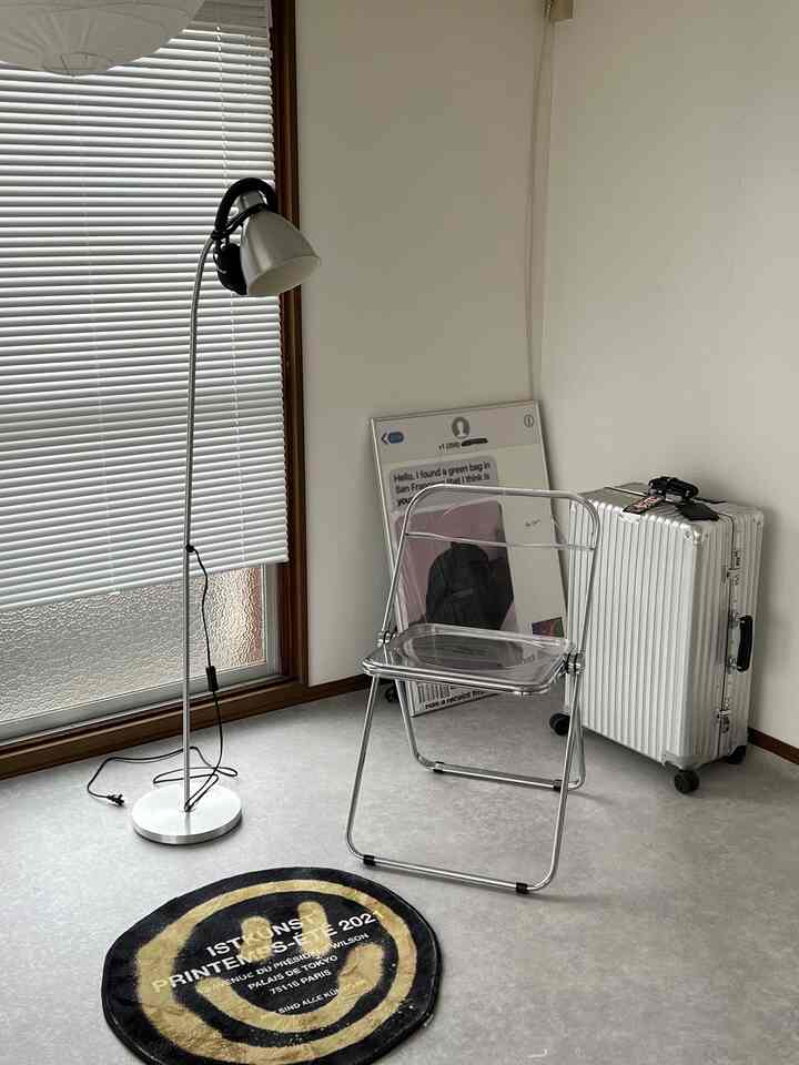 Gray floor and white walls define this studio apartment featuring a transparent stool and a floor lamp, creating a minimalistic vibe