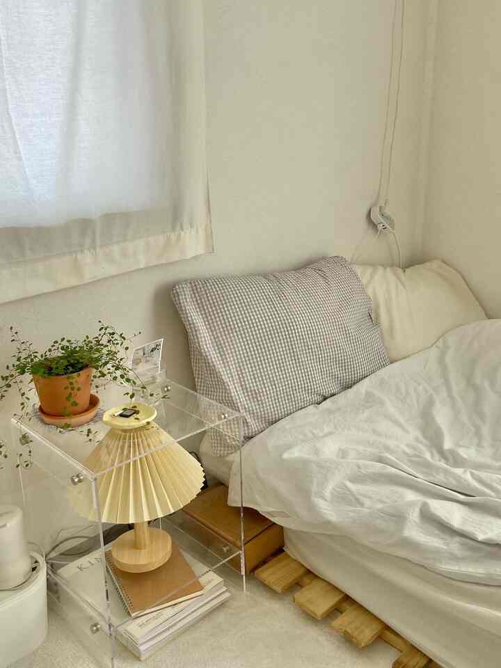 白とナチュラルカラーの寝室、透明なサイドテーブルとランプが置かれた印象的で落ち着いたインテリア