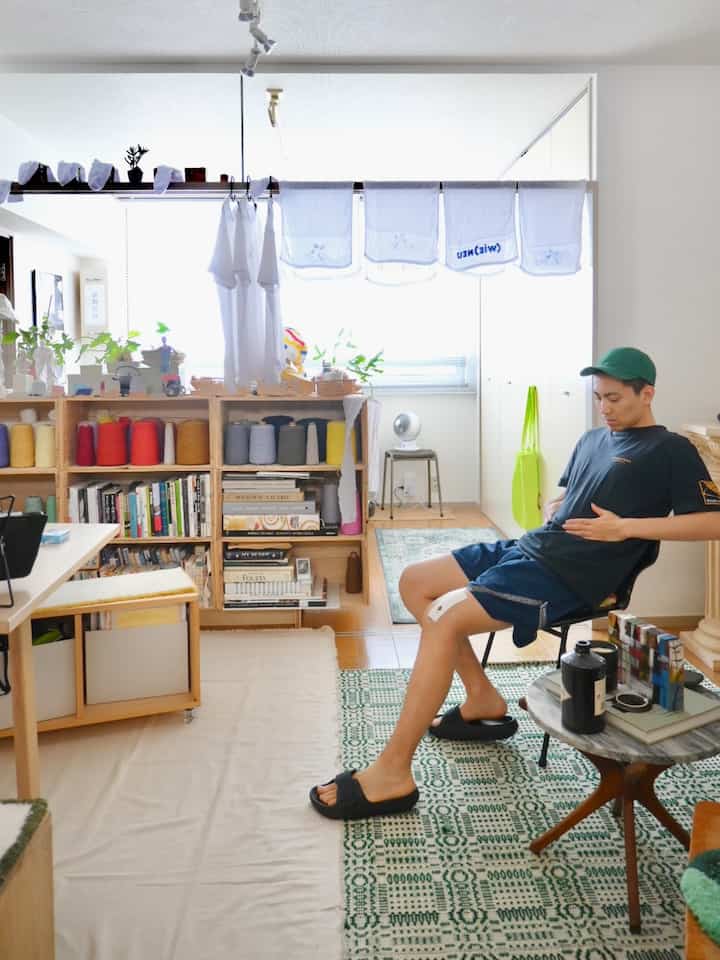 Natural-tone 6-tatami living room with wooden bookshelf and rug, featuring a seated person creating a relaxed atmosphere