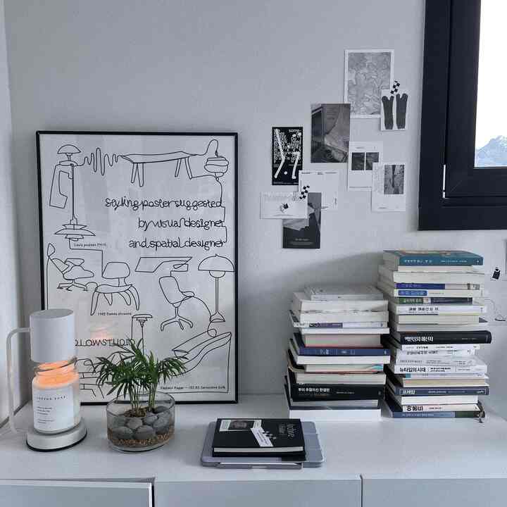 Minimalist study space in white and black tones, featuring stacks of books, a candle, and a small plant on a clean white sideboard