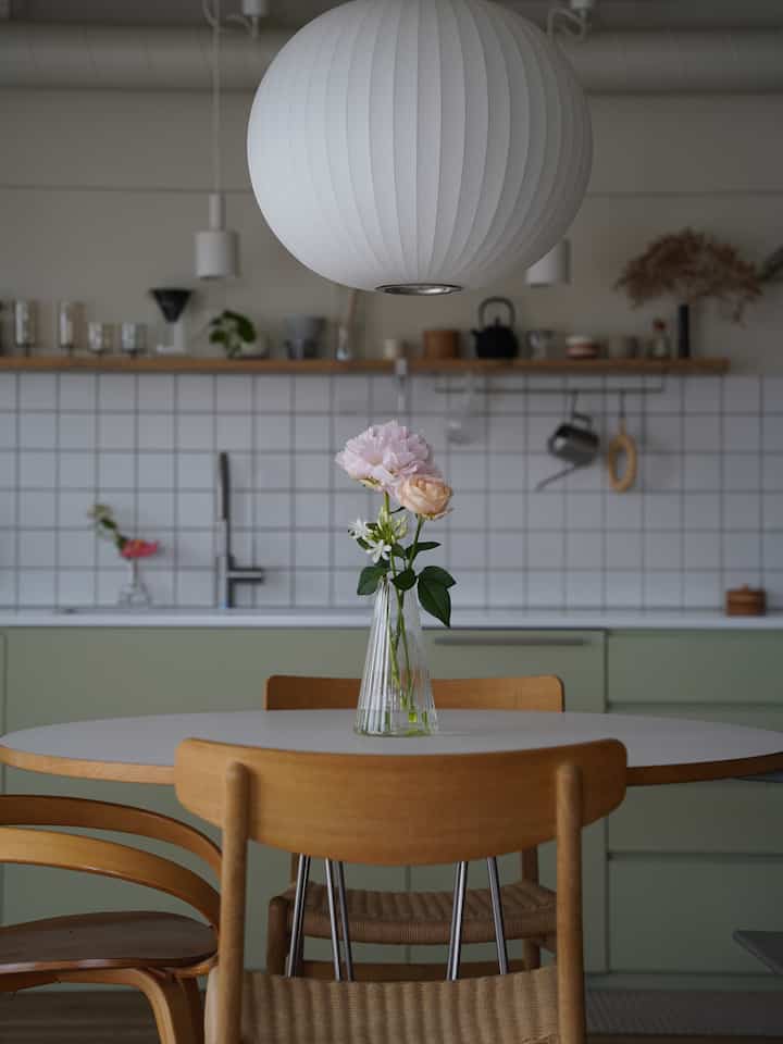 White and wood-tone dining room featuring a round table with flower vase and pendant light, presenting a natural atmosphere