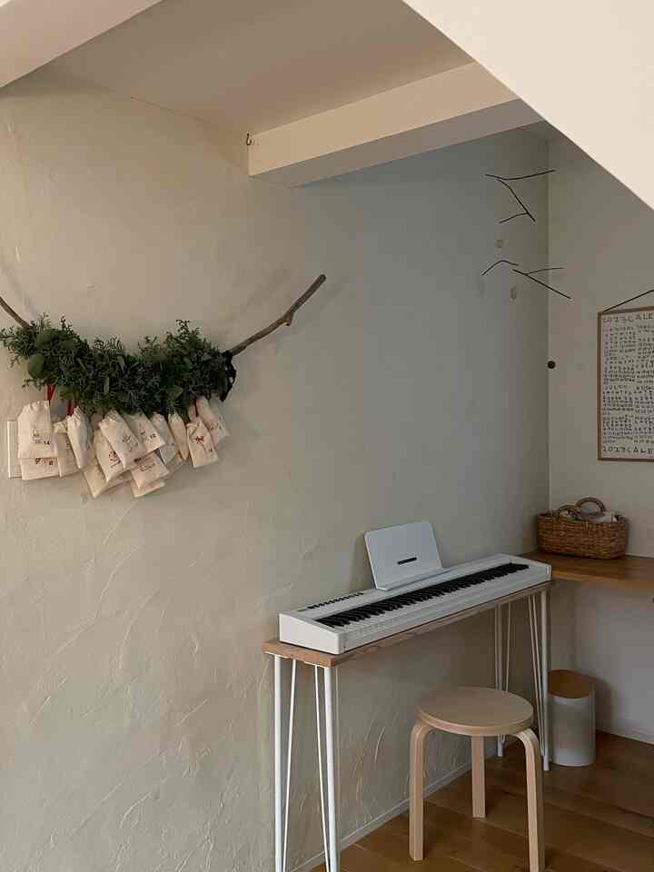 Natural beige-toned small room featuring an advent calendar hanging on the wall and a digital piano with stool, creating a warm atmosphere