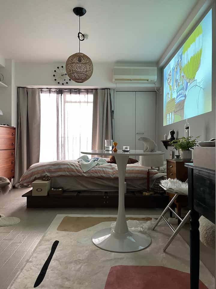 Neutral-toned bedroom featuring a low bed at center, round table in front, and animated projection on the wall creating cozy atmosphere