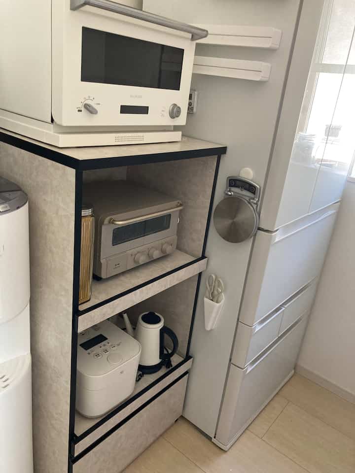 白を基調としたキッチンの一角、電子レンジやトースターオーブンが置かれたコンパクトな収納スペースが配置されたモダンなインテリア