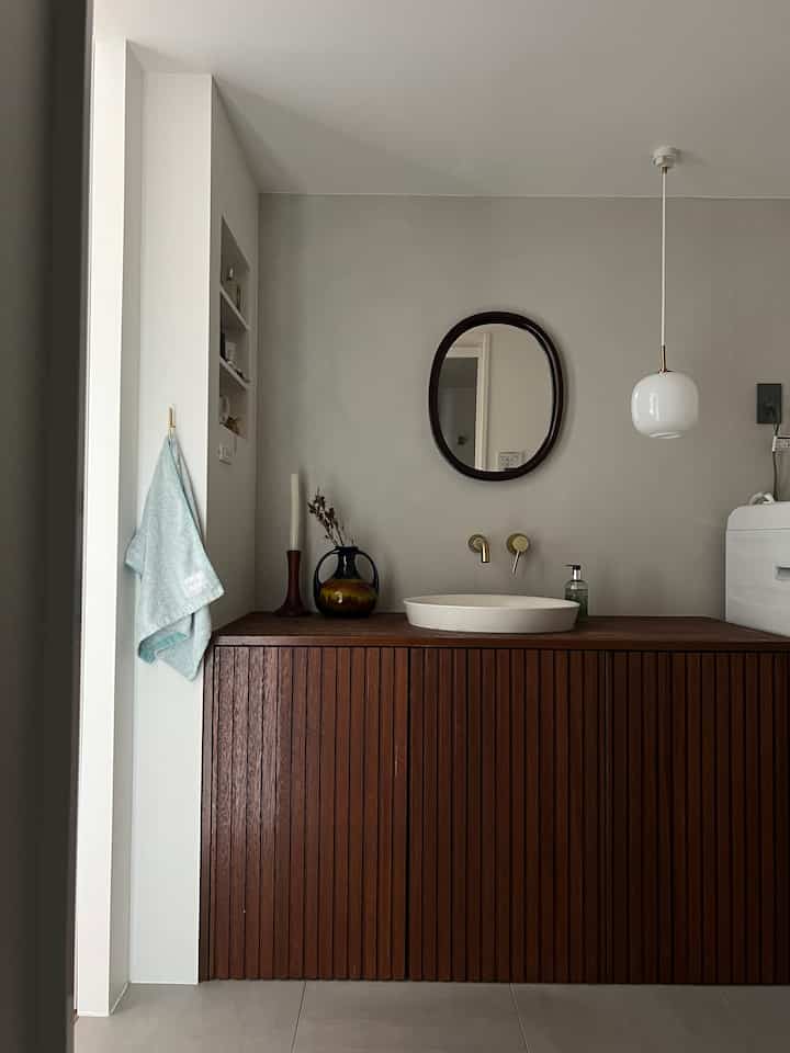 ナチュラルカラーのバスルーム、曲木の鏡と木製収納が配置された落ち着いた雰囲気のインテリア