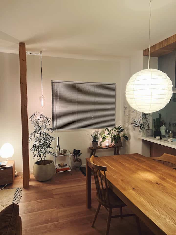 暖かみのある木目調と間接照明が調和した静かなダイニング、木製の食卓と植物が配置された落ち着いた空間