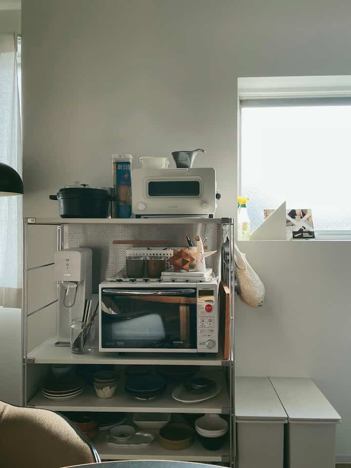 白を基調としたキッチンの一角、整理された収納棚と家電、ナチュラルカラーの調理器具が配置された雰囲気のあるインテリア