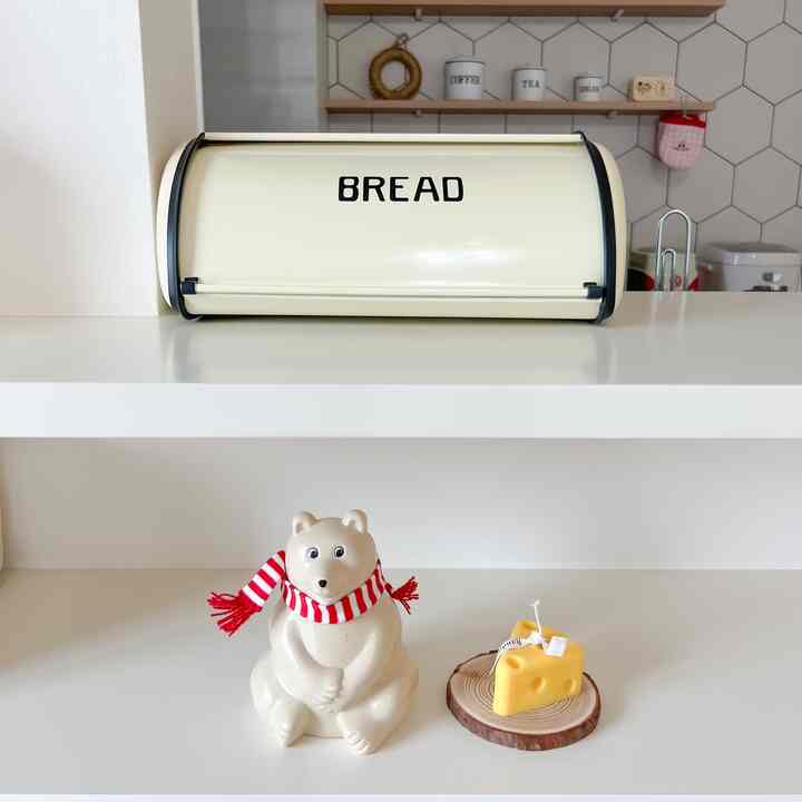 アイボリー色のキッチン棚にベージュのパンケースと赤いマフラーをしたクマのオブジェが配置されたシンプルなキッチンのインテリア