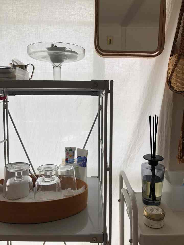 白いカーテン背景にシルバーの棚とワイングラス、黒のディフューザーが配置されたシンプルで整った空間