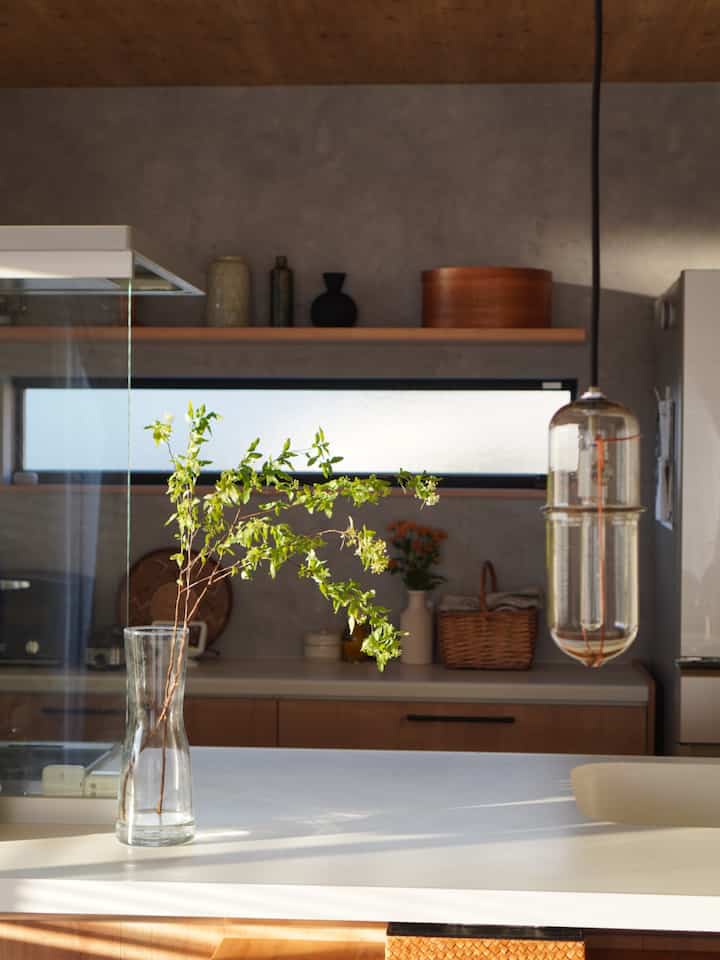 ナチュラルな木目調と白が調和するキッチン、透明な花瓶に植物が飾られたミニマルで雰囲気のあるインテリア