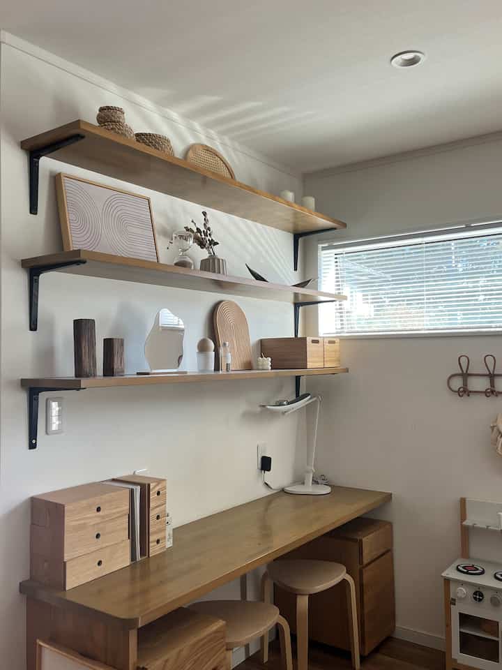 白い壁と木目調のデスク、スツール、壁棚が配置されたナチュラルモダンなホームオフィスの空間
