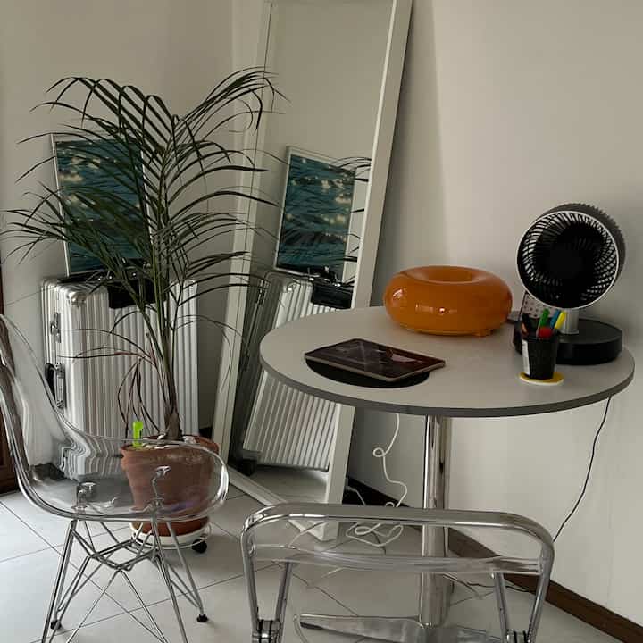 白い壁と透明な椅子があるコンパクトなワンルーム、観葉植物と円形のダイニングテーブルが配置されたモダンな空間