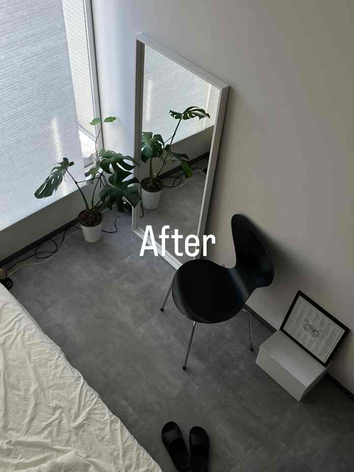 ホワイトとグレーのトーンの寝室、黒い椅子と大きな鏡、緑の植物が配置されたモダンでシンプルなインテリア