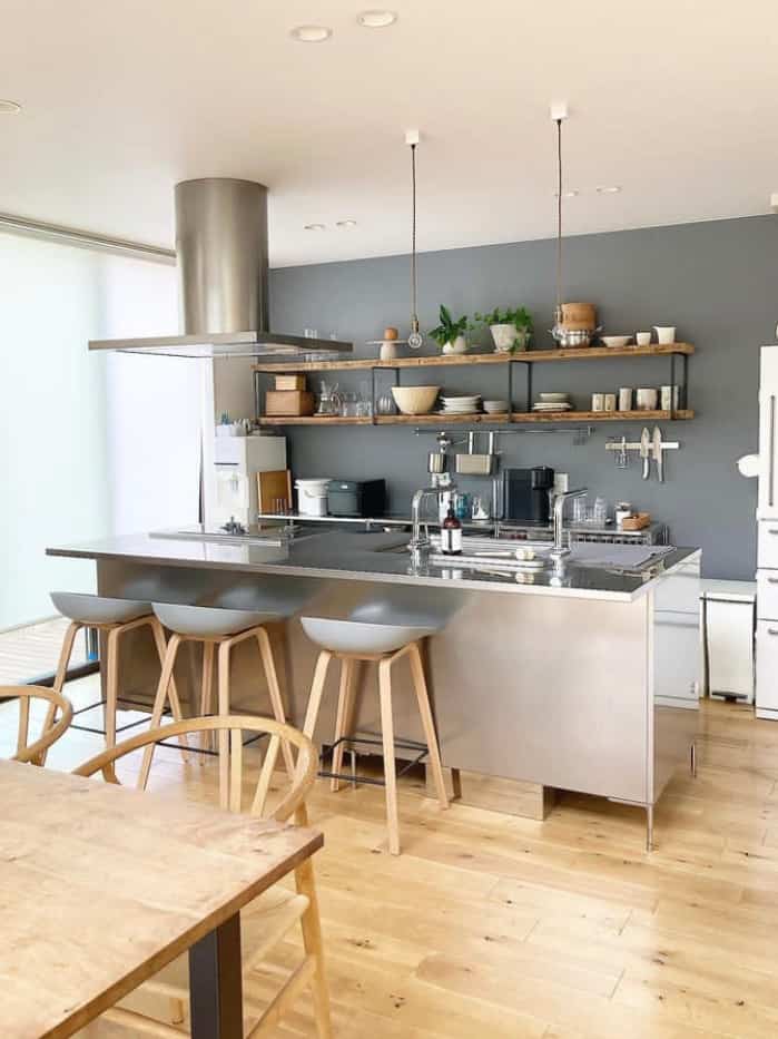 Wood tone flooring and gray wall create a harmonious dining room and open kitchen with stools and dining chairs in a natural modern space