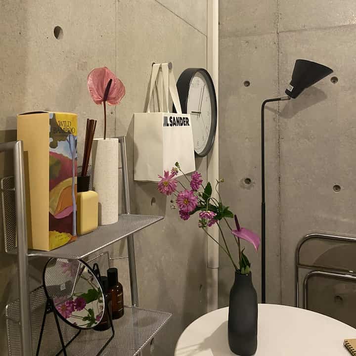 Modern interior with gray concrete walls, floor lamp, wall clock, and a vase on a small table in a minimalistic space