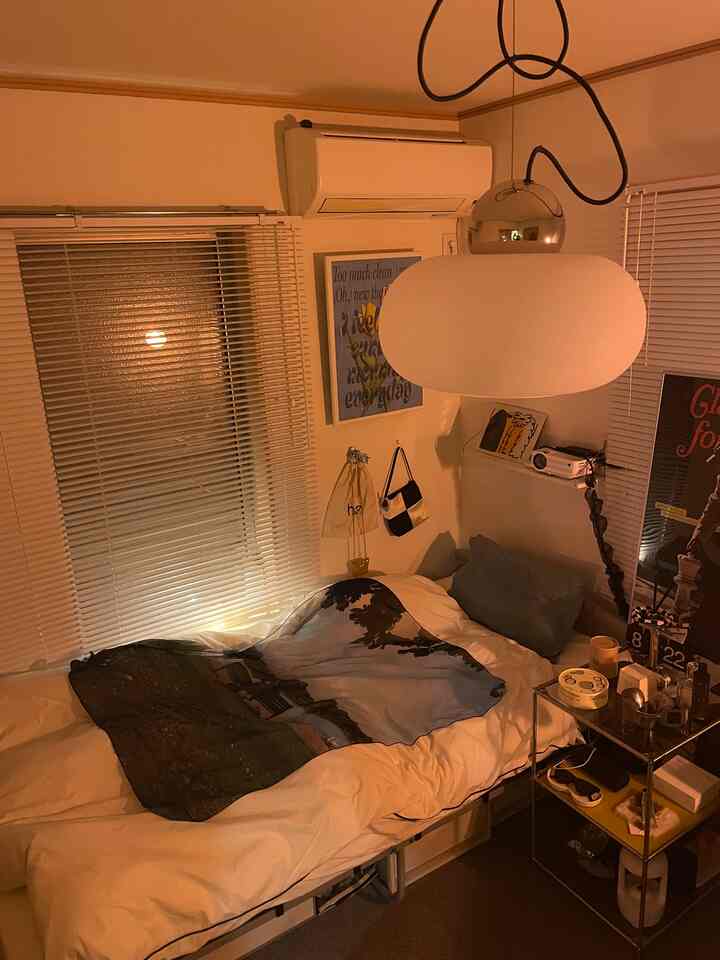 柔らかなオレンジ色の照明が漂う一人用寝室、ペンダントライトとブラインドが配された雰囲気あるインテリア