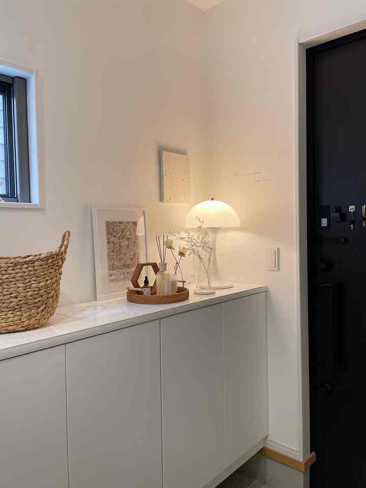 White-toned entrance featuring a clean storage cabinet with a reproduct style table lamp and basket, creating a simple natural space