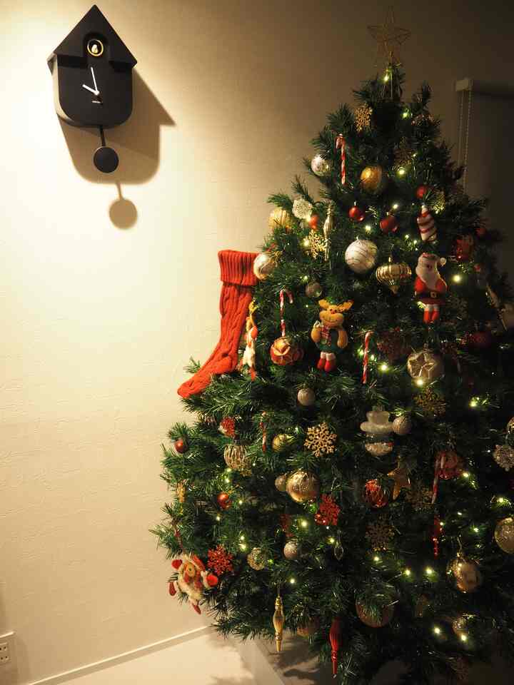 Warm-toned space featuring a gold and red decorated Christmas tree next to a beige wall adorned with a black cuckoo wall clock