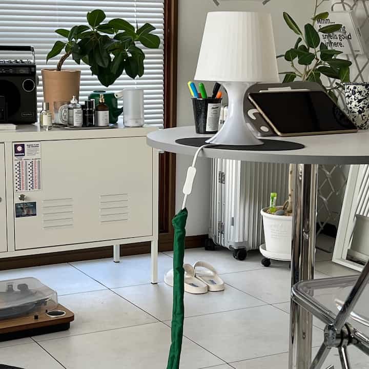 白とグレーのトーンのリビング、中央に丸テーブルとランプ、横に収納キャビネットが配置されたシンプルな印象的な空間