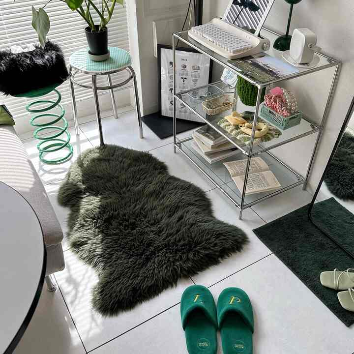 明るい白いタイル床と透明な棚があるナチュラルグリーン調のリビング、猫が乗った緑のスツールと緑のスリッパが見える居心地の良い清潔な空間